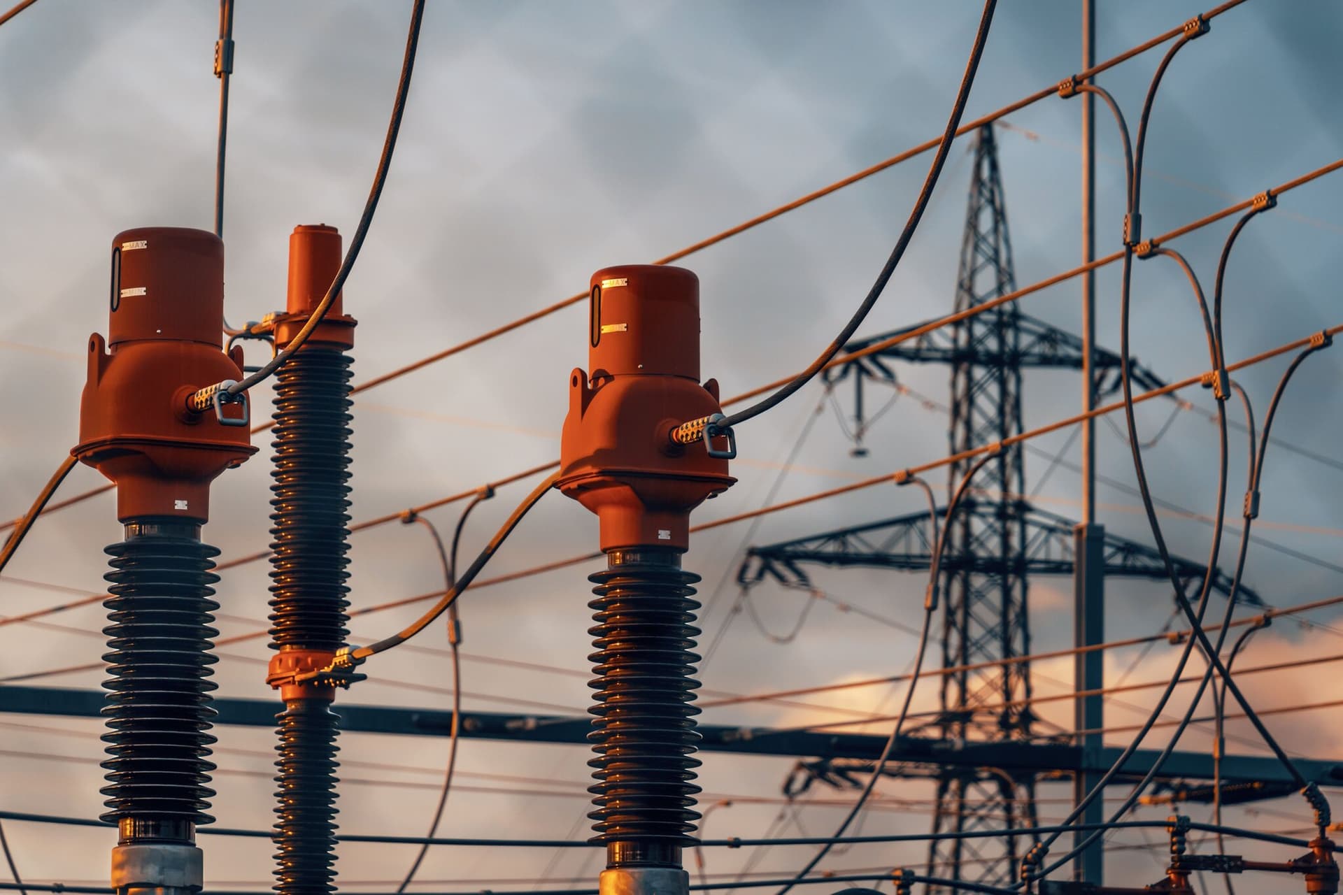 High-voltage transformer bushings against a dusk sky, a transmission pylon behind